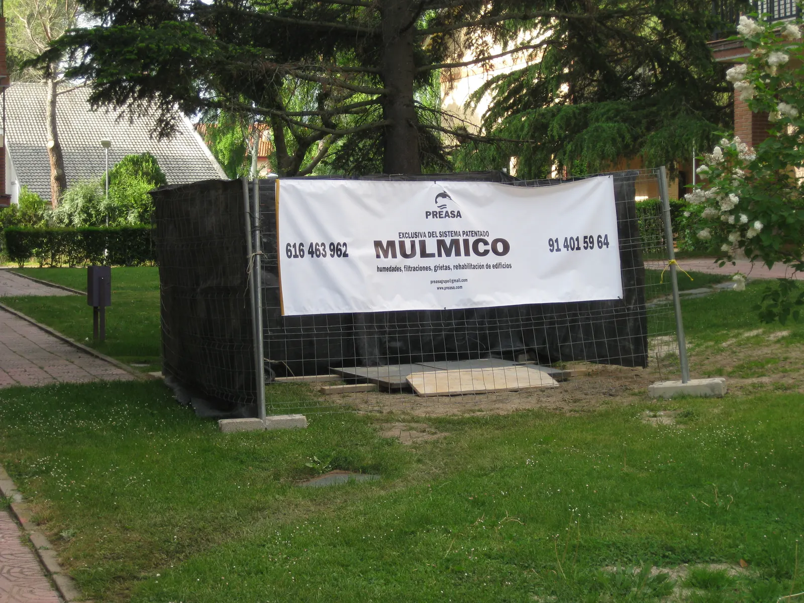 Zona de obra vallada en el jardín de la urbanización con la lona del Sistema Mulmico